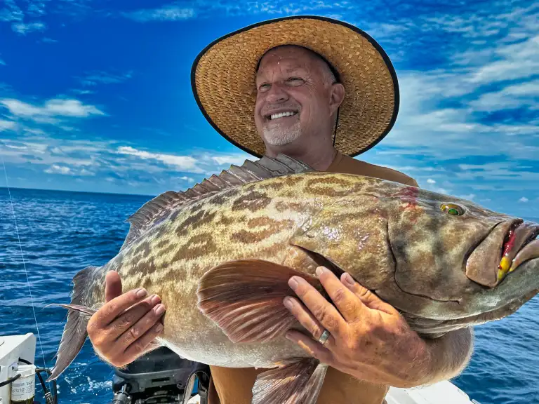 A guest in a straw hat holds a broomtail grouper landed near the rock structure off Nosara.