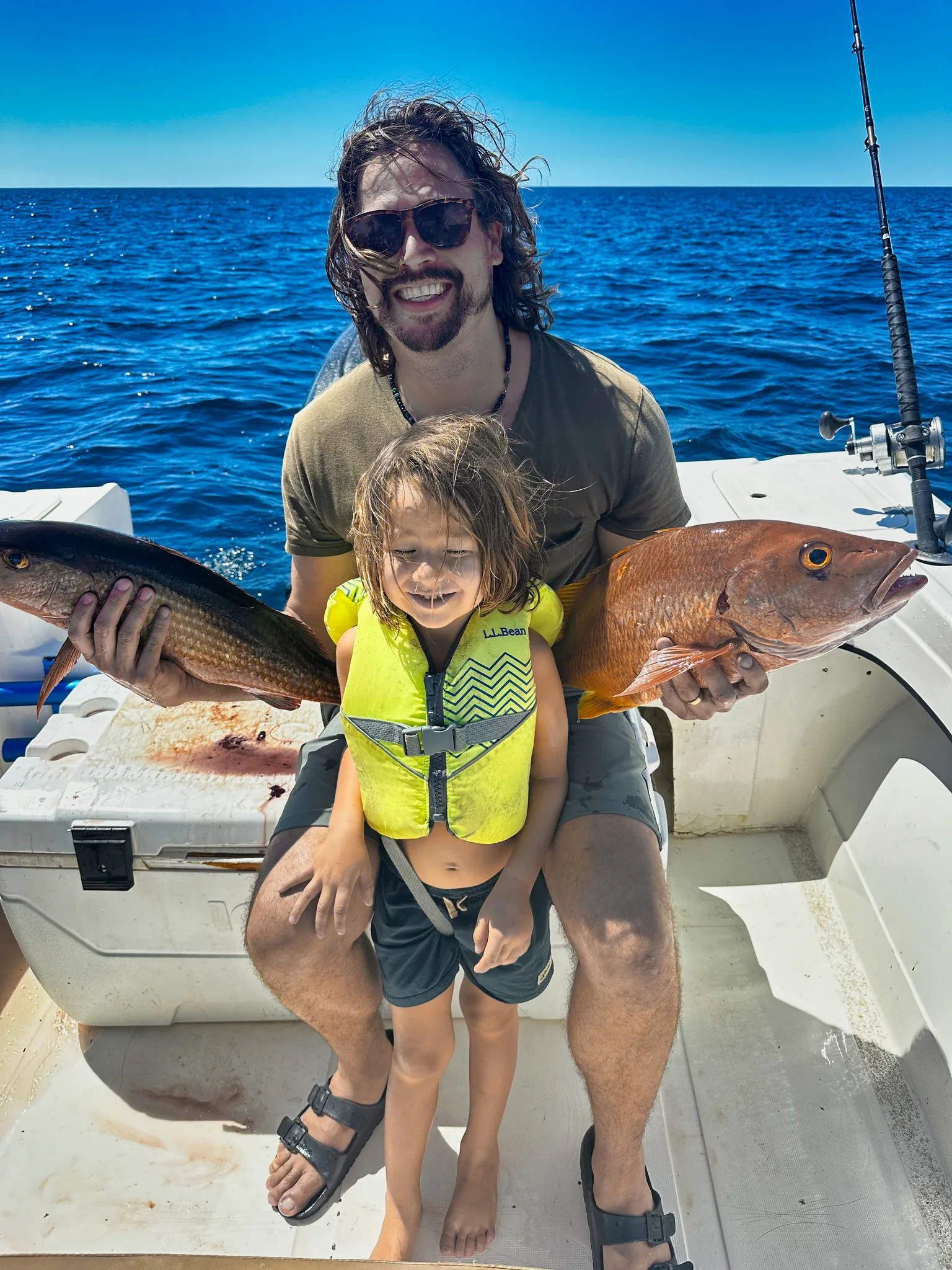 Family inshore fishing near Nosara – father and daughter with snappers A guest holds two snappers while his daughter in a life jacket smiles on the boat deck.