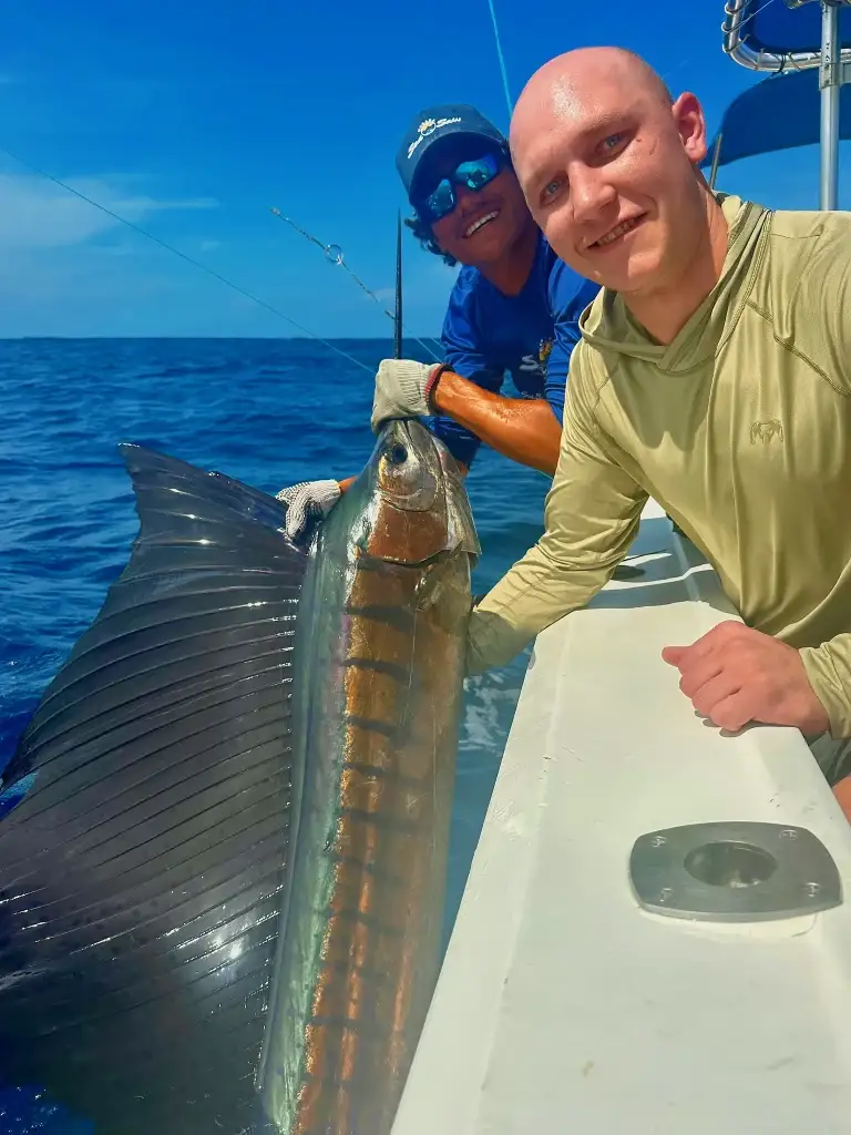 An angler and a crew member hold a sailfish beside the boat before releasing it.