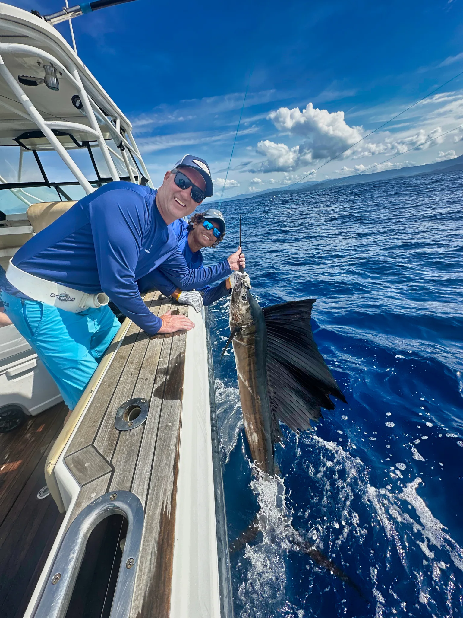 Two guests lean over the transom holding a sailfish in the water before release.