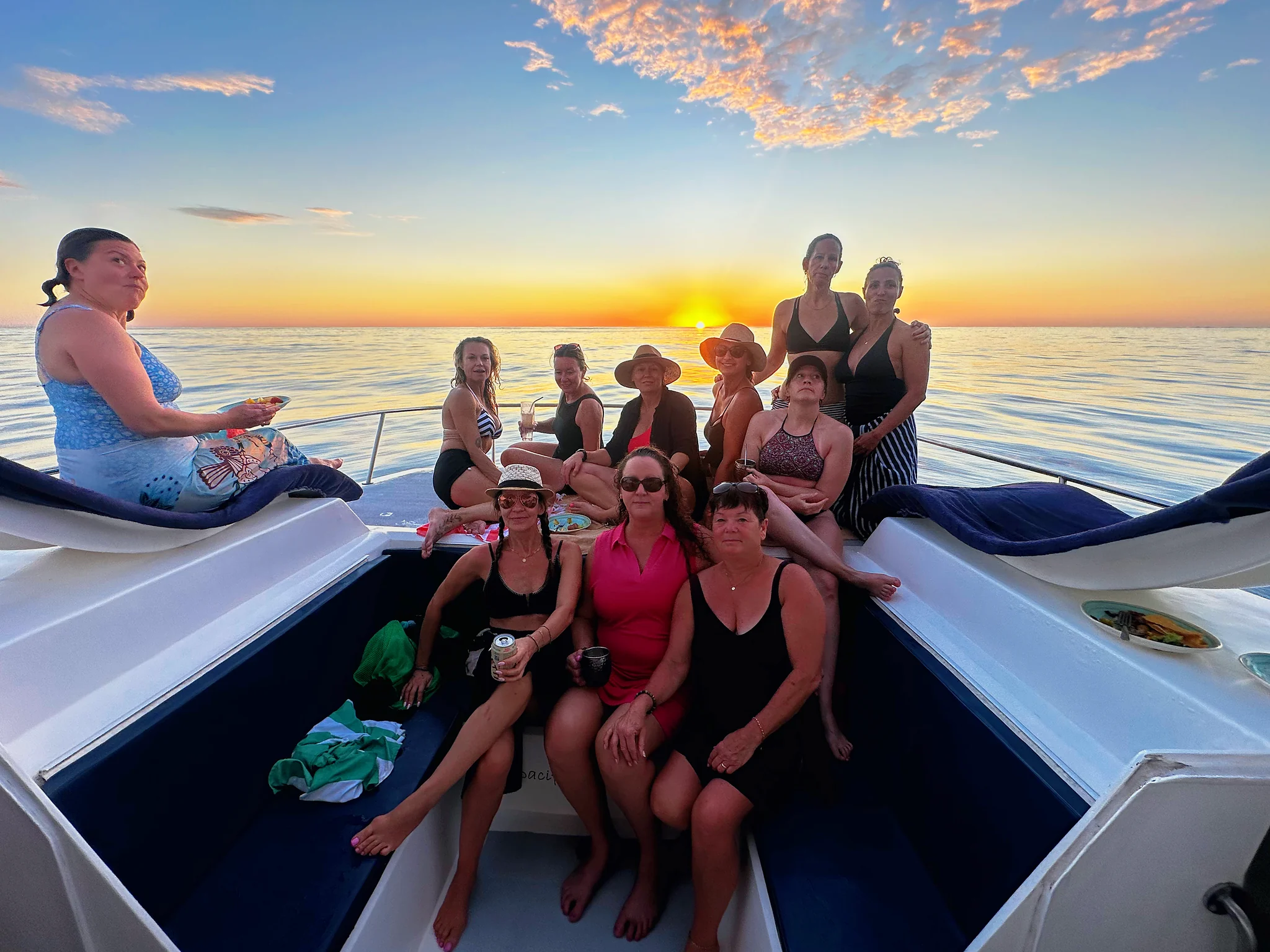 Group on the bow at golden hour | Pacific Dream Nosara A group of guests smiles on the catamaran bow as the sun sets on the horizon.