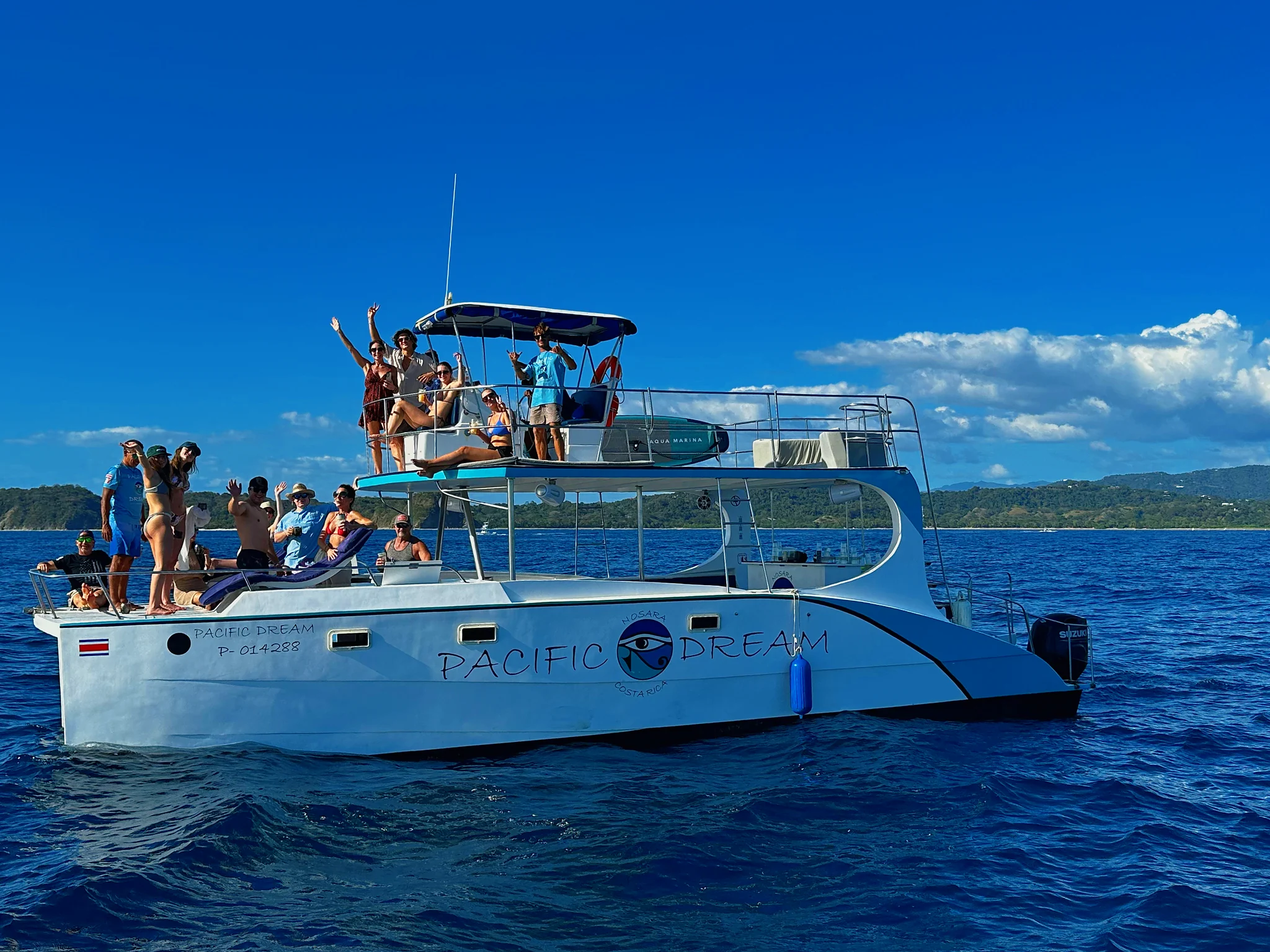 Guests waving from the upper and lower decks of the Pacific Dream catamaran off the Nosara coast.