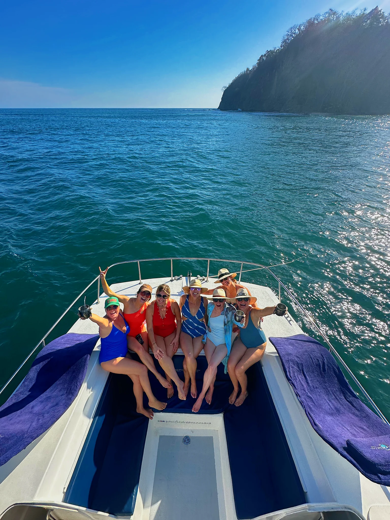 Guests sit together on the catamaran bow as it approaches a forested headland.